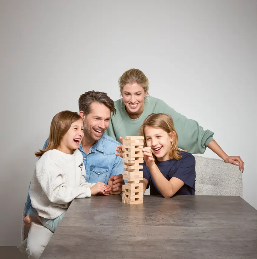 Glückliche Familie spielt gemeinsam ein Geschicklichkeitsspiel am modernen Esstisch. Eltern und Kinder lachen und verbringen Zeit zusammen. Wohnliche Atmosphäre mit hochwertigem Tisch und gemütlichem Zuhause Ambiente.